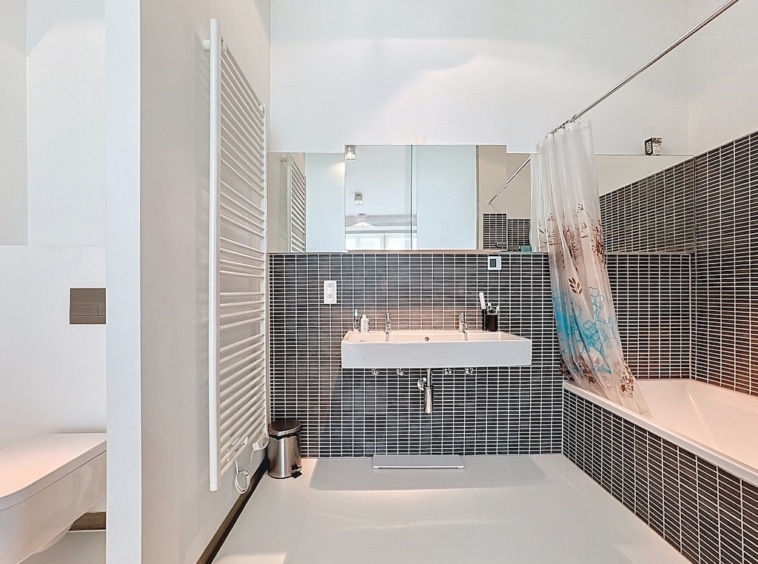 Salle de bain moderne, baignoire arrondie, murs blancs, carrelage noir, lavabo minimaliste, miroir élégant.