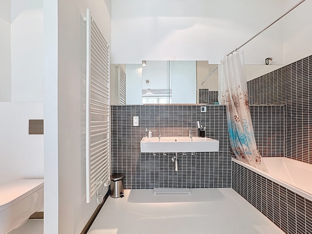 Salle de bain moderne, baignoire arrondie, murs blancs, carrelage noir, lavabo minimaliste, miroir élégant.