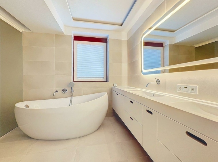 Salle de bain moderne avec baignoire ovale, éclairage doux, miroir éclairé et design minimaliste.