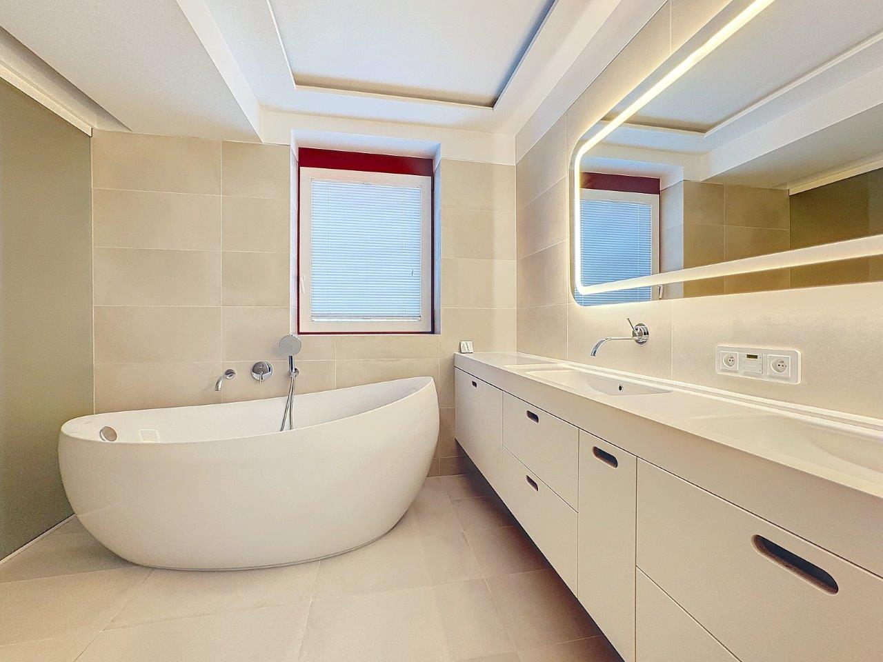 Salle de bain moderne avec baignoire ovale, éclairage doux, miroir éclairé et design minimaliste.