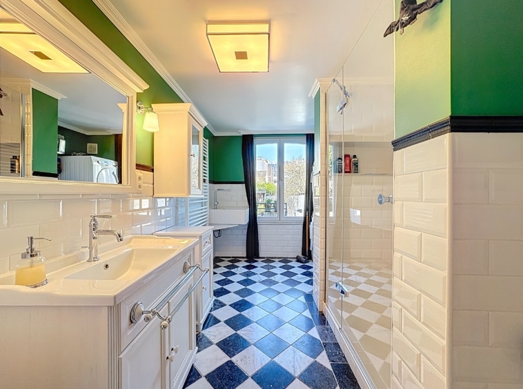 Salle de bain moderne avec double vasque, douche en verre, murs verts et sol à carreaux.