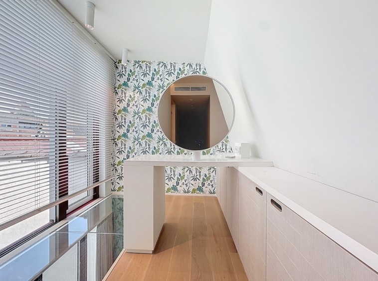 Salle de bain moderne minimaliste avec miroir circulaire, lumière naturelle, touches florales et bois chaud.