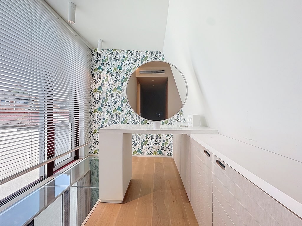 Salle de bain moderne minimaliste avec miroir circulaire, lumière naturelle, touches florales et bois chaud.