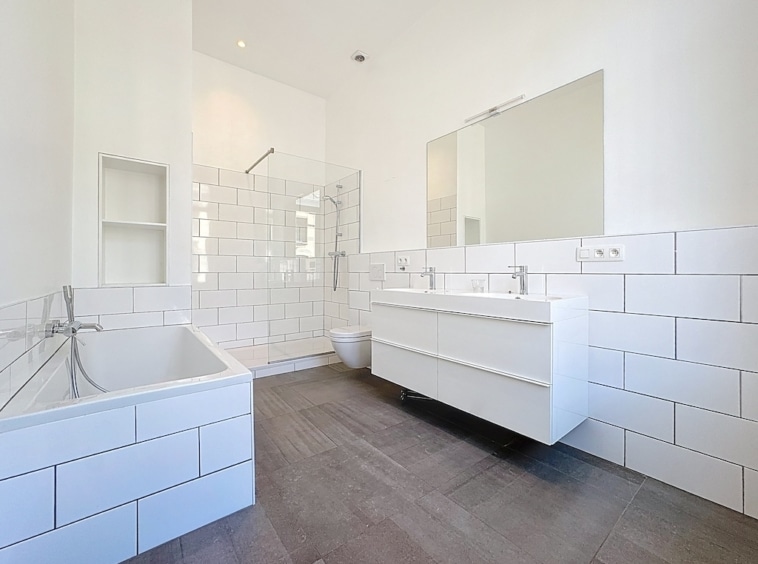 Salle de bain moderne avec baignoire, douche à l’italienne et double lavabo blanc.
