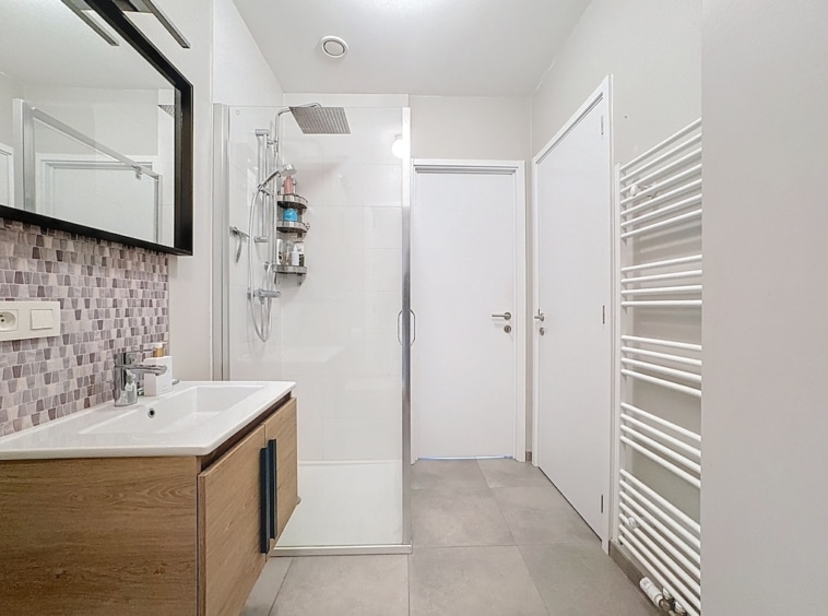 Salle de bain moderne minimaliste avec douche à l’italienne, grand miroir et mobilier en bois.