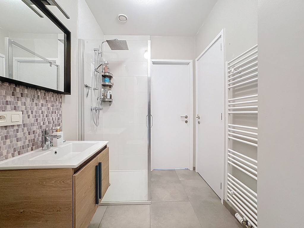 Salle de bain moderne minimaliste avec douche à l’italienne, grand miroir et mobilier en bois.