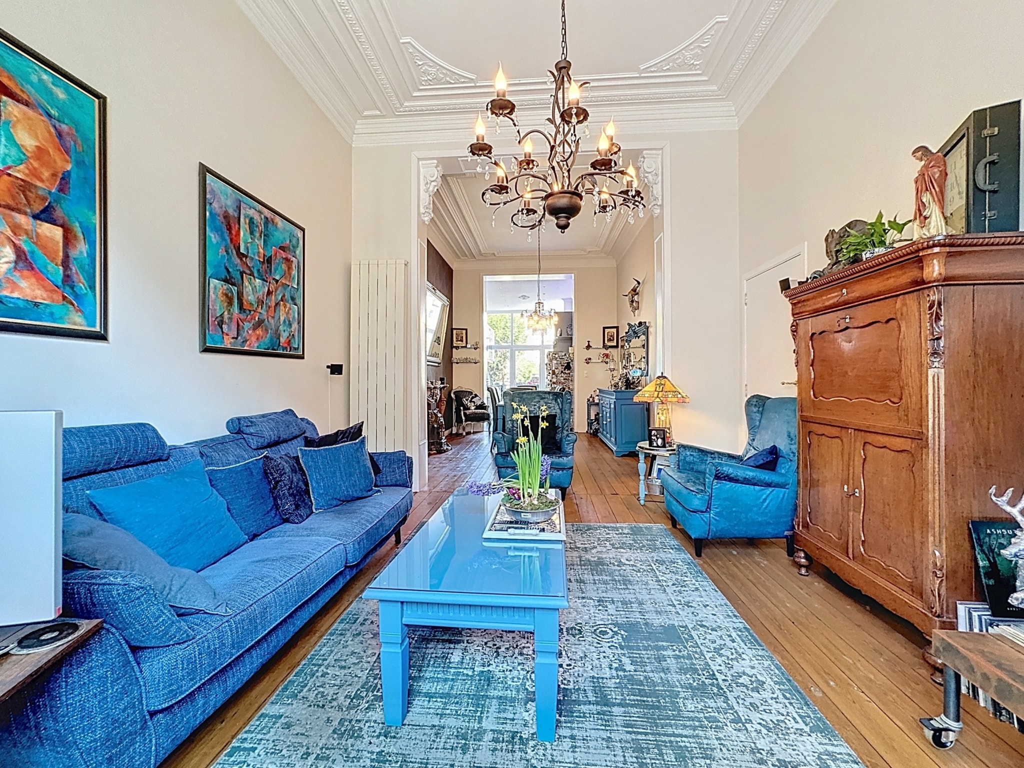 Salon cosy en bleu avec meubles élégants, œuvres d’art colorées et éclairage chaleureux.