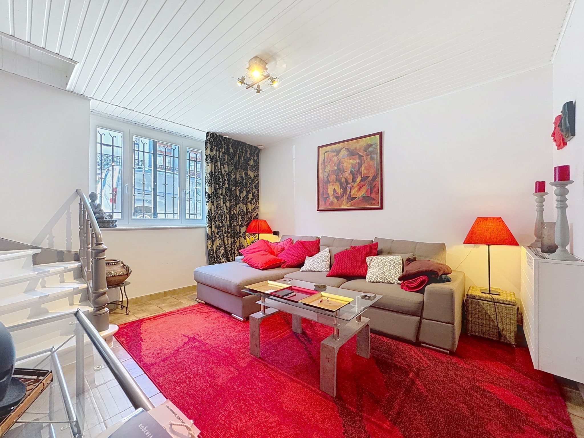 Salon moderne chaleureux avec canapé gris, coussins rouges, tapis moelleux et décoration colorée.