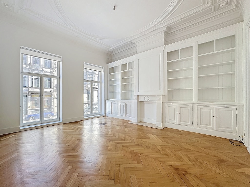 Salon lumineux avec parquet en chevrons, murs neutres, hauts plafonds et étagères intégrées élégantes.