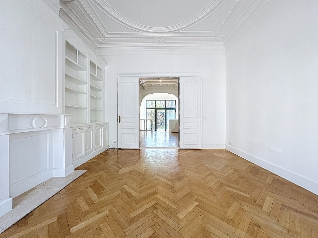 Salon lumineux minimaliste avec parquet en hampe, moulures élégantes et portes vitrées.