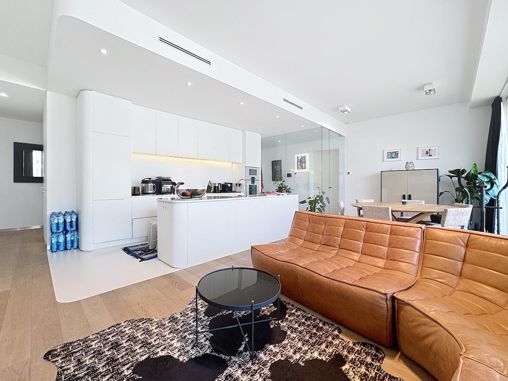 Salon moderne avec cuisine ouverte, espace repas en bois, canapé en cuir et décoration végétale.