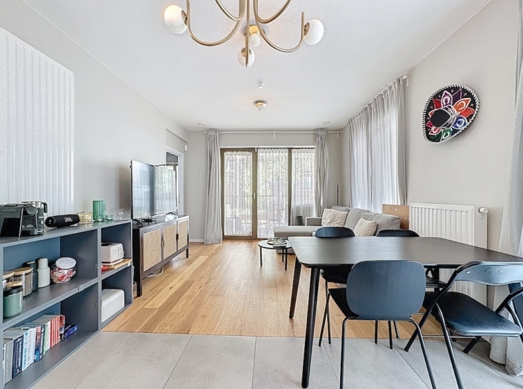 Salon moderne lumineux avec coin repas en bois clair, canapé gris et décoration minimaliste élégante.