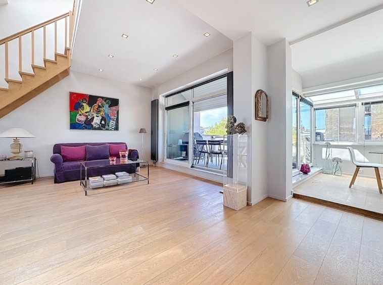 Salon moderne lumineux avec canapé violet, terrasse ensoleillée et mobilier minimaliste.