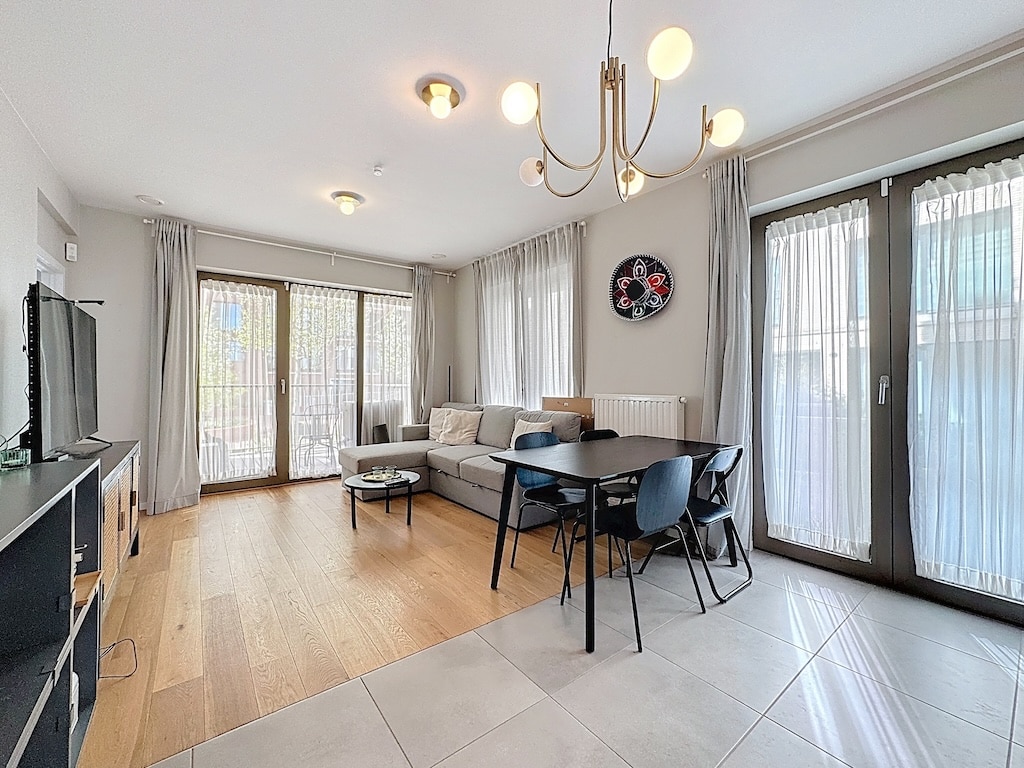 Salon contemporain lumineux avec canapé gris, table noire et grandes fenêtres élégantes.