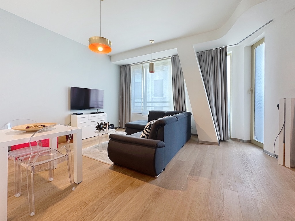Salon moderne minimaliste avec canapé noir, espace repas blanc, grande fenêtre et éclairage chaleureux.