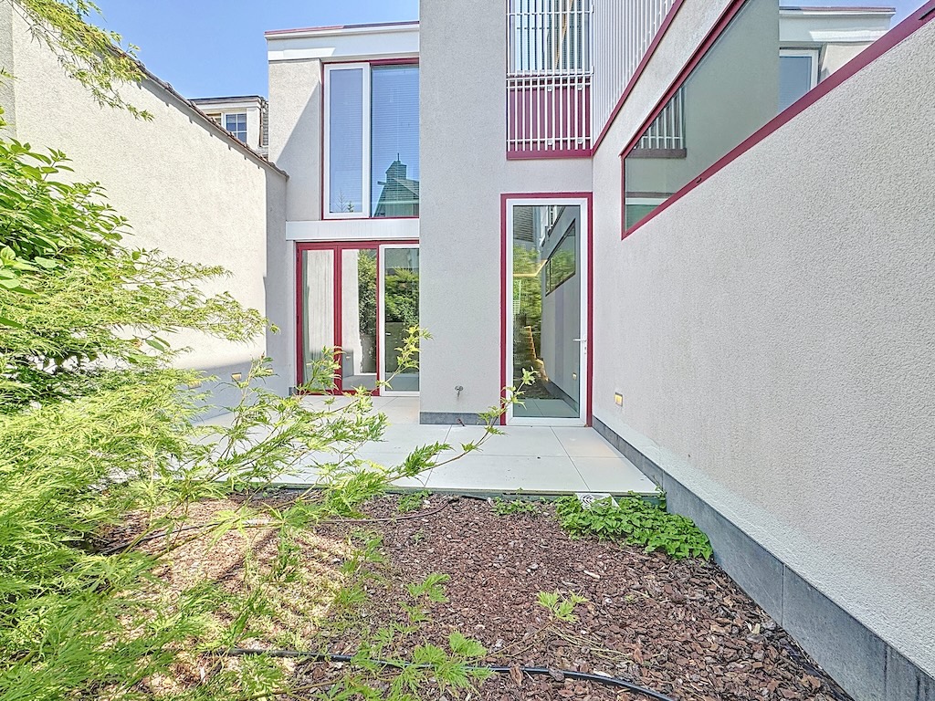 Maison moderne avec grandes fenêtres vitrées, façade neutre et jardin paysager élégant.