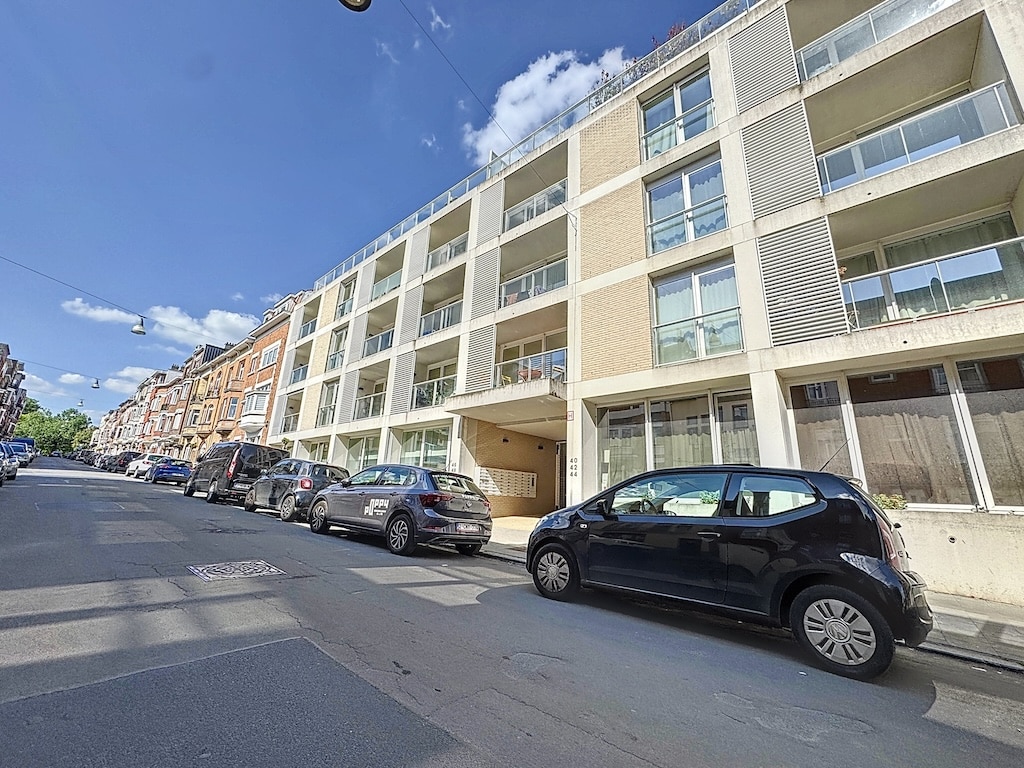 Apartment moderne avec grandes fenêtres et balcons en centre-ville animé, sous ciel bleu ensoleillé.