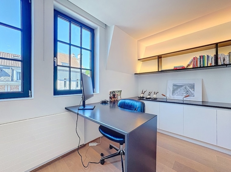 Bureau moderne lumineux avec fauteuil bleu, étagères intégrées et sol en bois chaleureux.