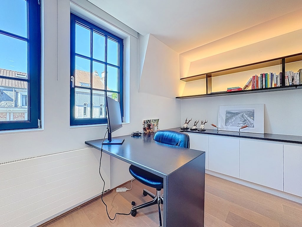 Bureau moderne lumineux avec fauteuil bleu, étagères intégrées et sol en bois chaleureux.