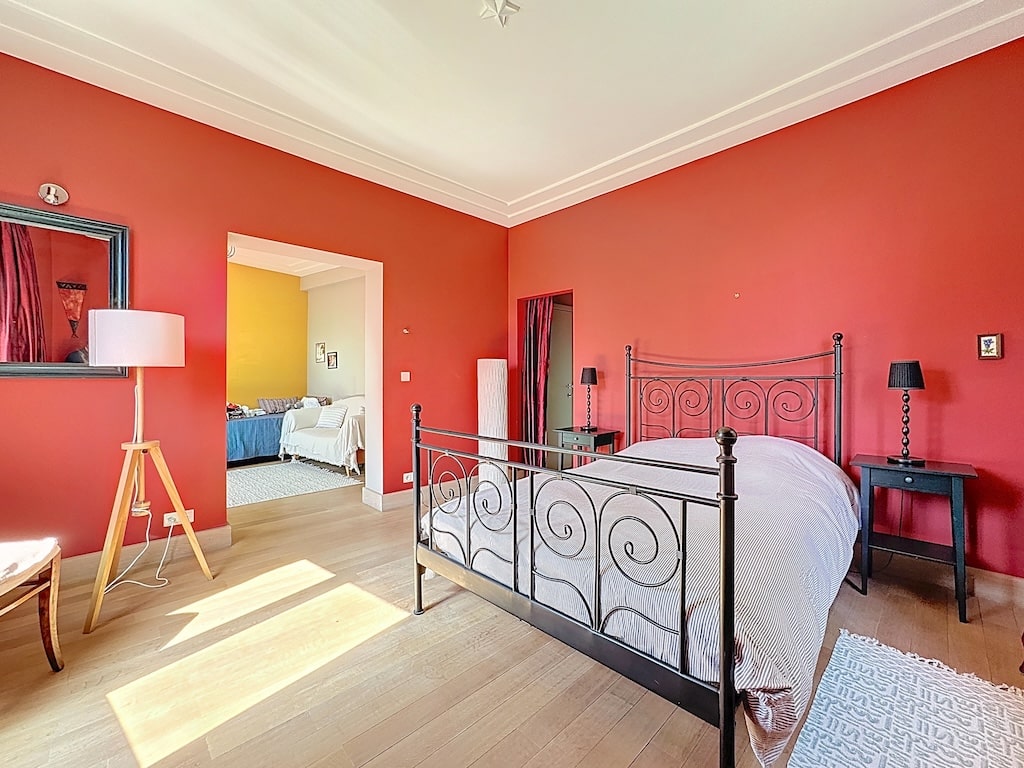 Chambre chaleureuse avec murs rouges, lit en fer noir, mobilier élégant et ambiance cosy.
