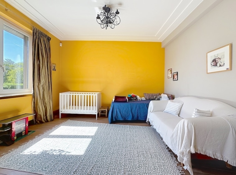 Chambre de bébé lumineuse avec lit blanc, canapé cosy, murs colorés et décoration chaleureuse