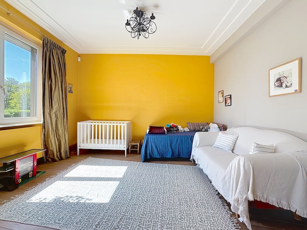 Chambre de bébé lumineuse avec lit blanc, canapé cosy, murs colorés et décoration chaleureuse