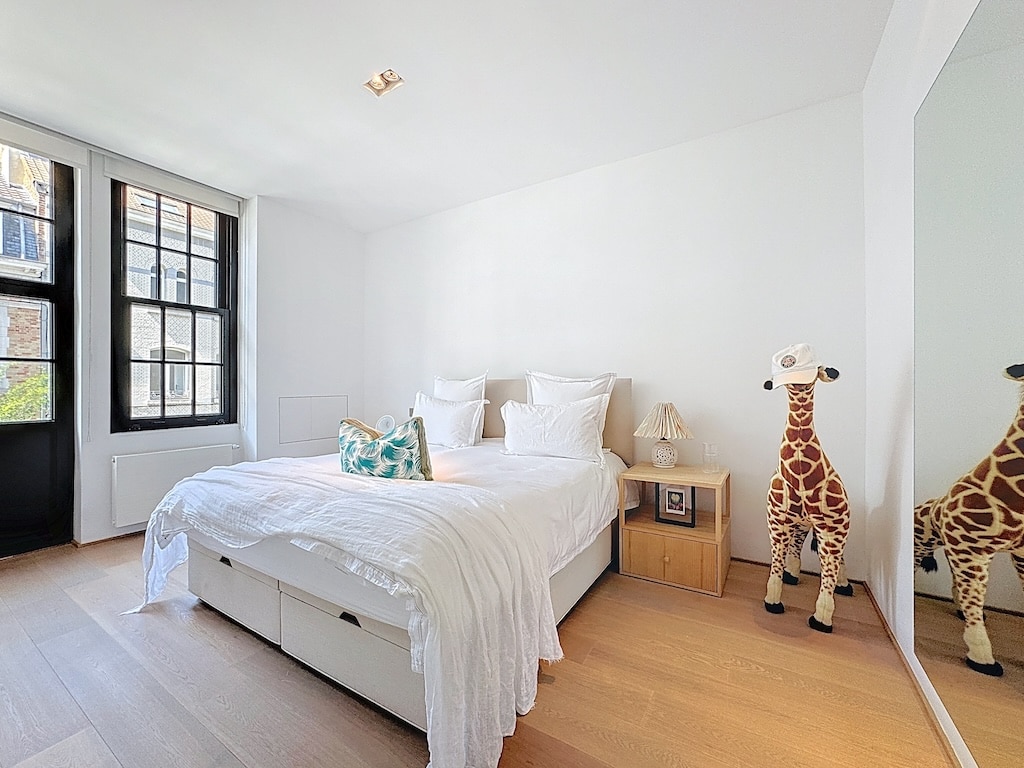 Chambre minimaliste lumineuse avec lit blanc, décor bois clair, girafes en figurines, ambiance apaisante.