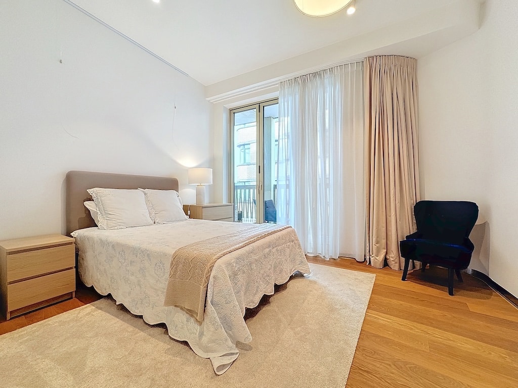 Chambre contemporaine apaisante avec lit élégant, lumière naturelle, fauteuil bleu et ambiance cozy.