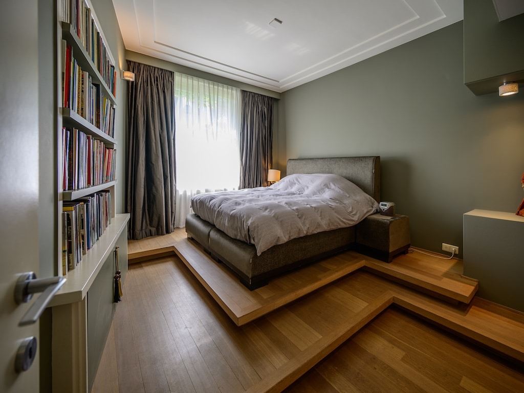 Chambre moderne avec lit king, lumière naturelle, décoration épurée et bibliothèque chaleureuse.