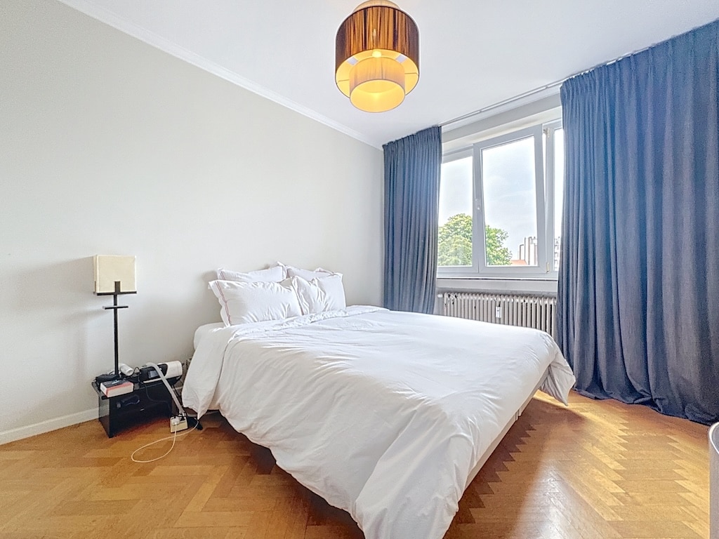 Chambre moderne et cosy avec parquet en chevrons, lumière naturelle et décoration épurée en blanc et bleu.