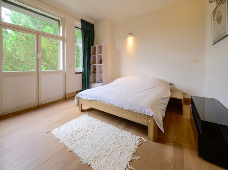 Chambre moderne et apaisante avec vue nature, lit minimaliste, parquet en bois, et décoration élégante.