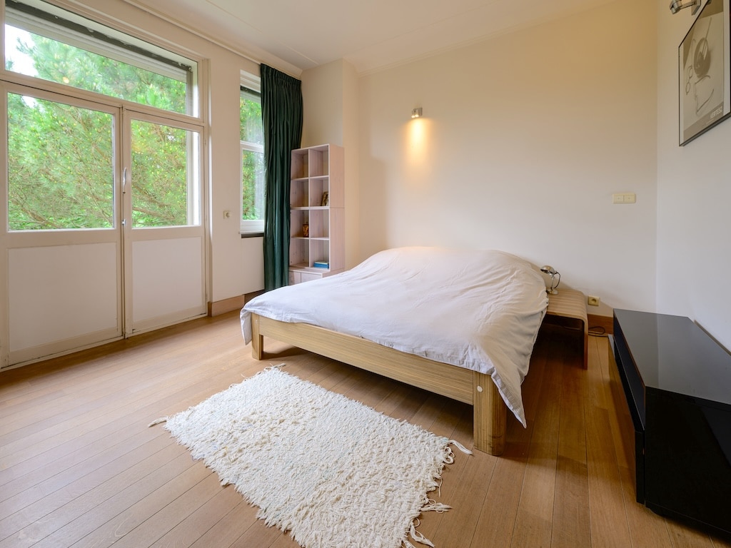Chambre moderne et apaisante avec vue nature, lit minimaliste, parquet en bois, et décoration élégante.