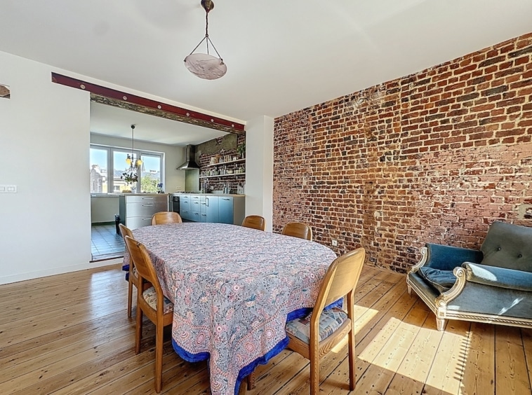 Coin repas chaleureux avec sol en bois, mur en briques, mobilier industriel, et fauteuil vintage bleu.