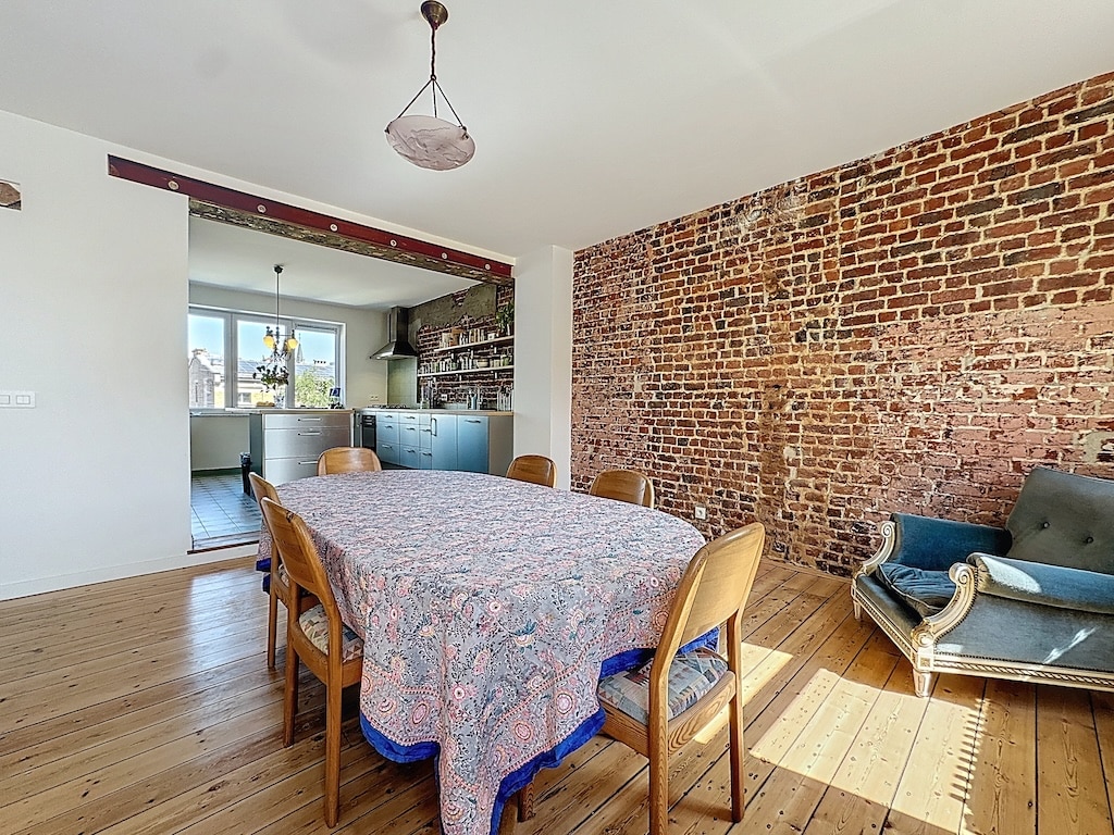 Coin repas chaleureux avec sol en bois, mur en briques, mobilier industriel, et fauteuil vintage bleu.