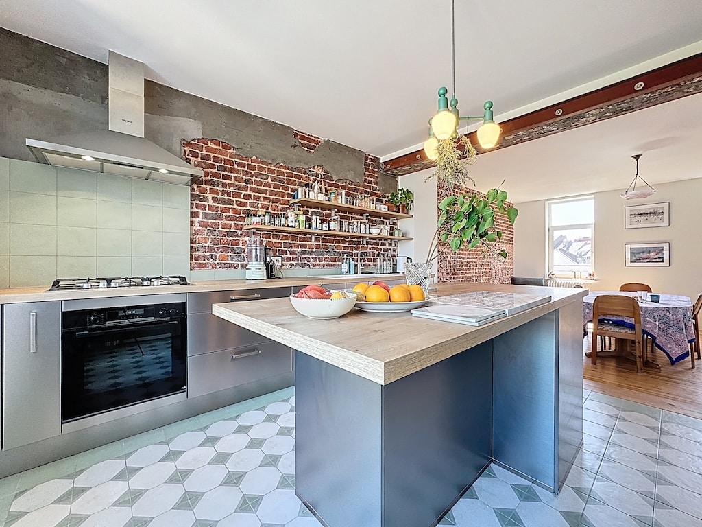 Cuisine moderne avec mur en briques, îlot en bois, éclairage design et sol en carrelage géométrique.