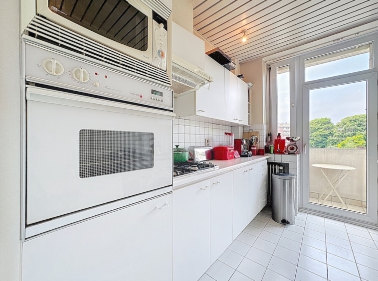Cuisine blanche moderne avec balcon et vue verdoyante, lumineux, élégante et conviviale.
