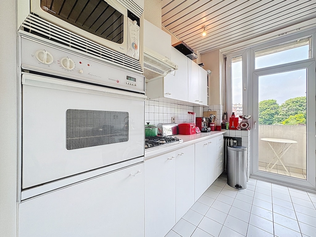 Cuisine blanche moderne avec balcon et vue verdoyante, lumineux, élégante et conviviale.