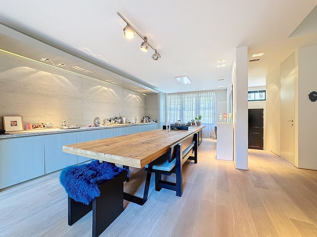 Cuisine moderne lumineuse avec table en bois, chaises noires, armoires bleu clair et éclairage intégré.