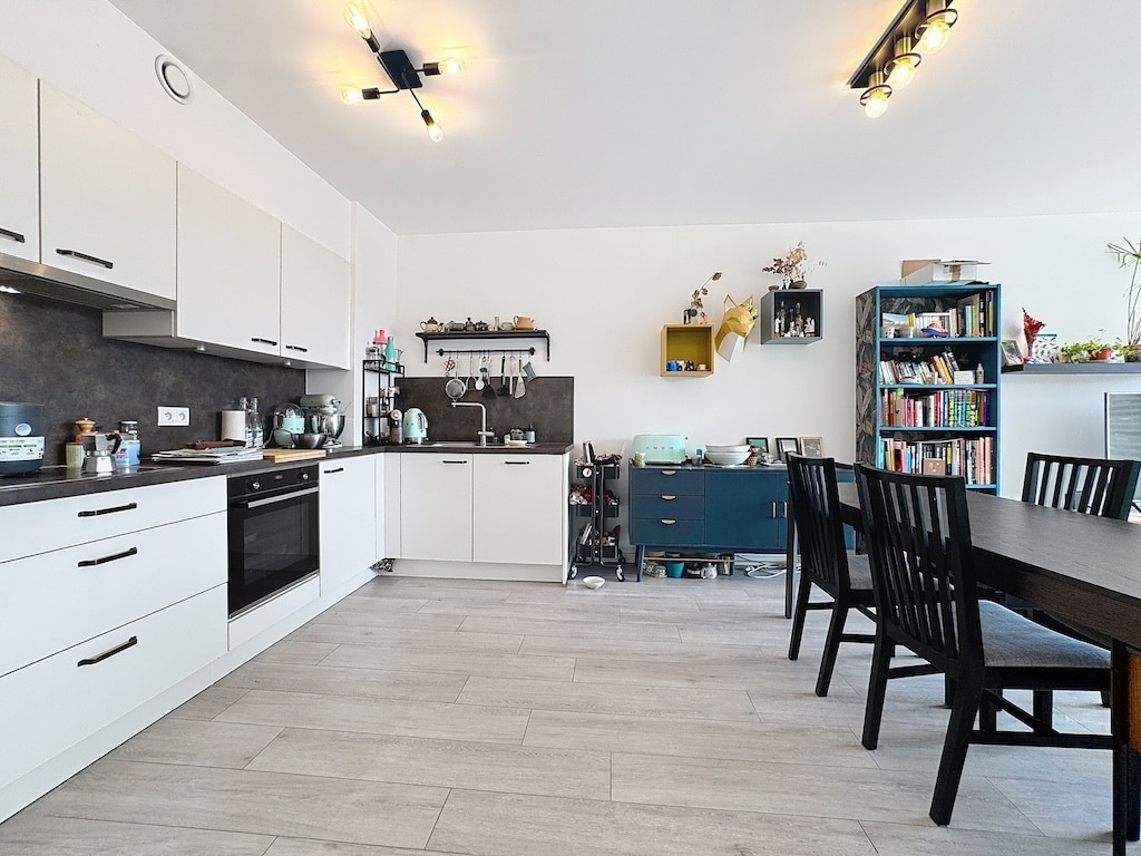 Cuisine moderne, chaleureuse, espace repas convivial avec mobilier blanc, noir, étagères décoratives et sol lumineux.