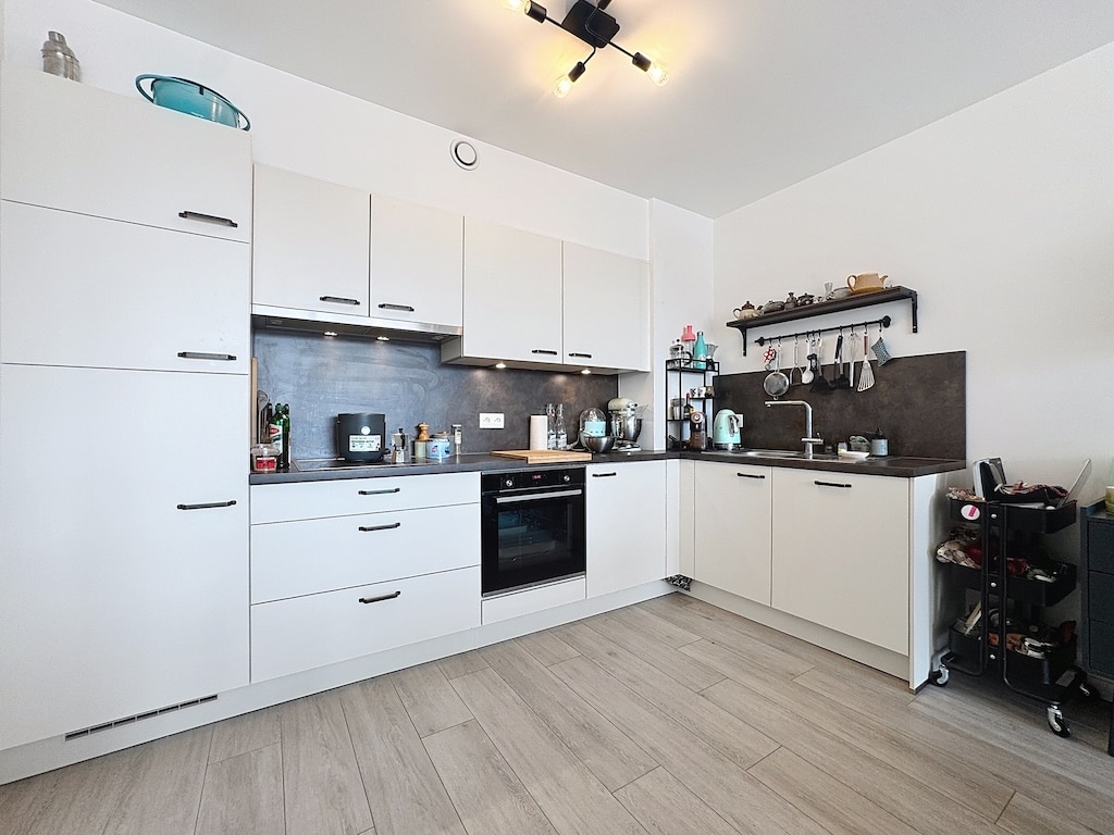 Cuisine moderne blanche, éclairee, équipée, avec plan de travail organisé, sol en bois clair.