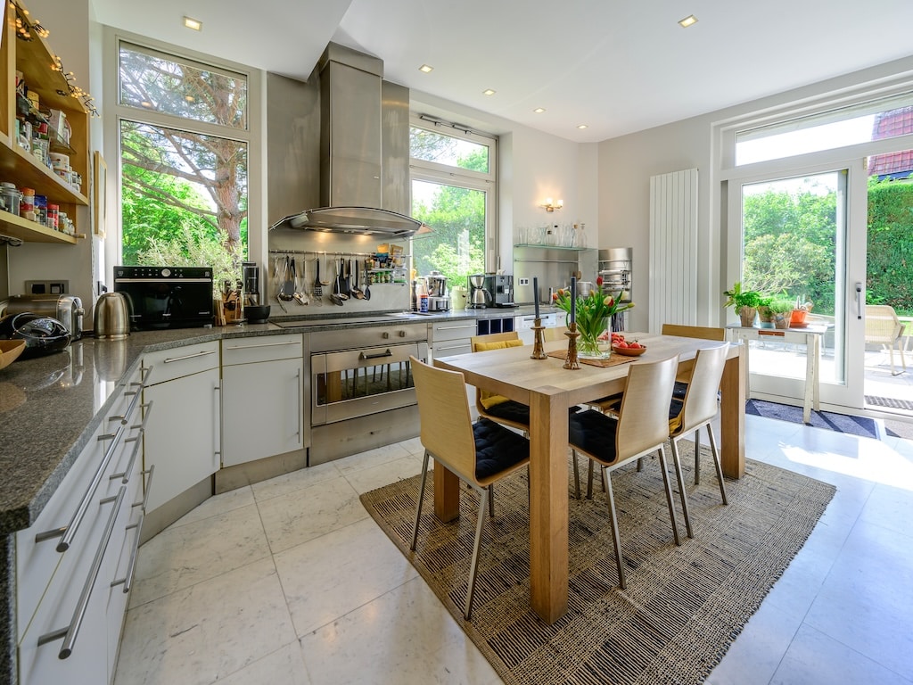 Cuisine moderne lumineuse avec espace repas en bois, appareils intégrés et accès patio verdoyant.