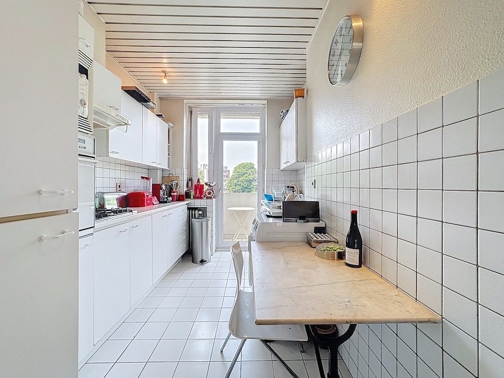 Cuisine moderne lumineuse avec coin repas en marbre, vue verte, style épuré et touches rustiques.