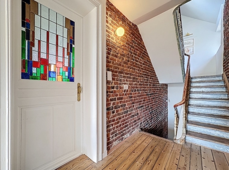 Entrée chaleureuse avec porte en Vitrail coloré, mur en briques et escalier en bois poli.