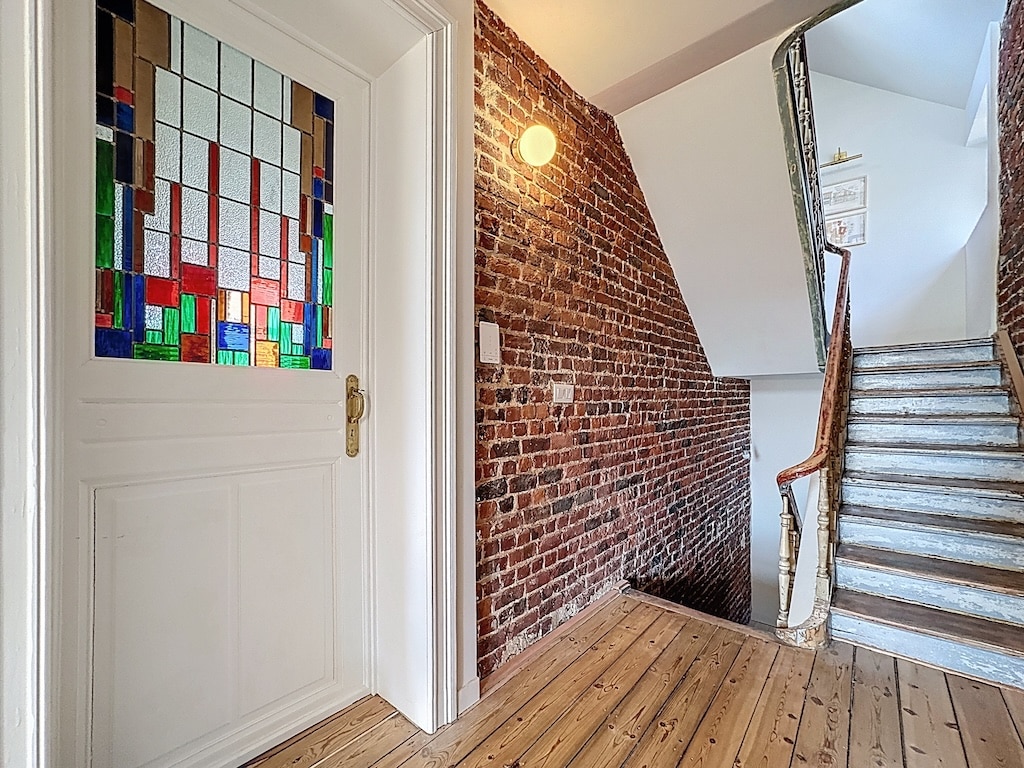 Entrée chaleureuse avec porte en Vitrail coloré, mur en briques et escalier en bois poli.