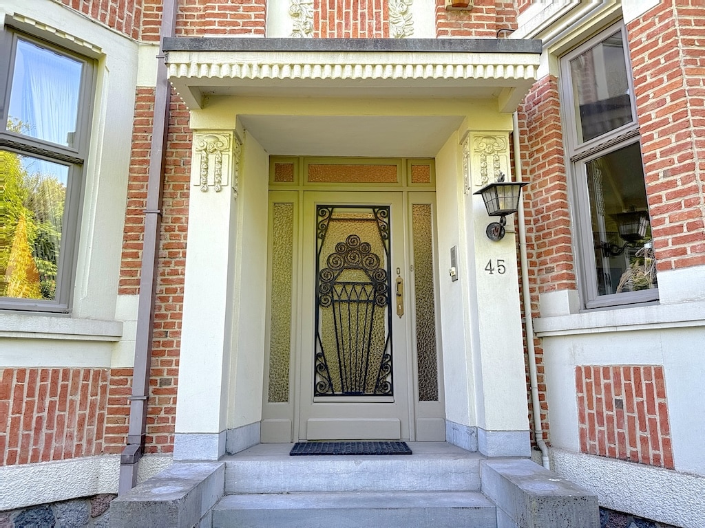 Entrée élégante avec porte en verre, fenêtres lumineuses, colonnes décoratives et terrasse en pierre.
