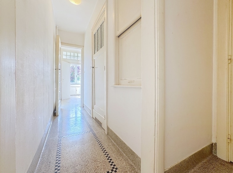 Hall moderne et lumineux avec murs blancs, sol terrazzo clair et ouverture sur l’extérieur.