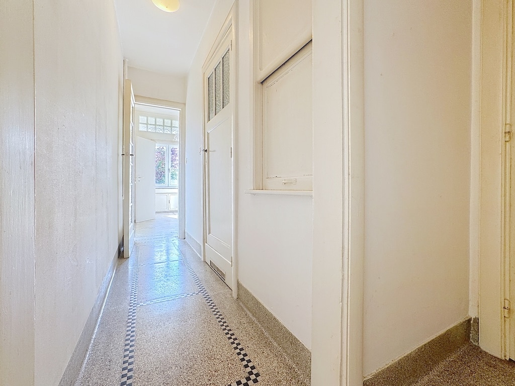 Hall moderne et lumineux avec murs blancs, sol terrazzo clair et ouverture sur l’extérieur.