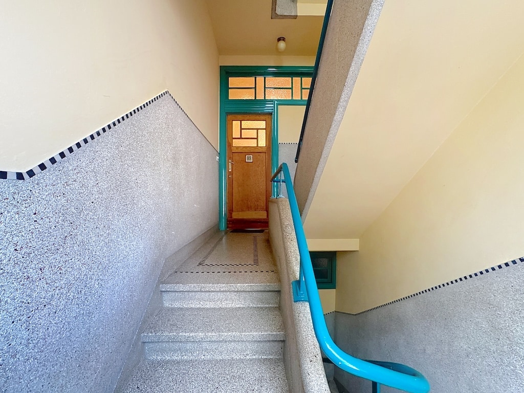 Escalier moderne en pierre avec balustrade turquoise menant à une porte en bois vitrée.