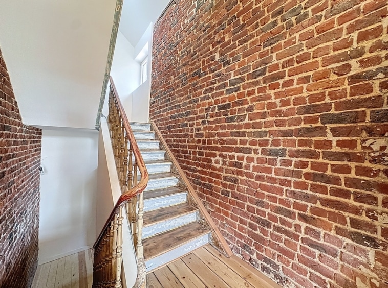Escalier en bois clair avec balustrade élégante dans un intérieur en briques chaleureuses.