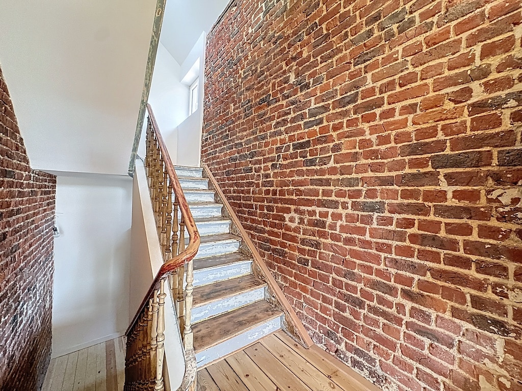 Escalier en bois clair avec balustrade élégante dans un intérieur en briques chaleureuses.